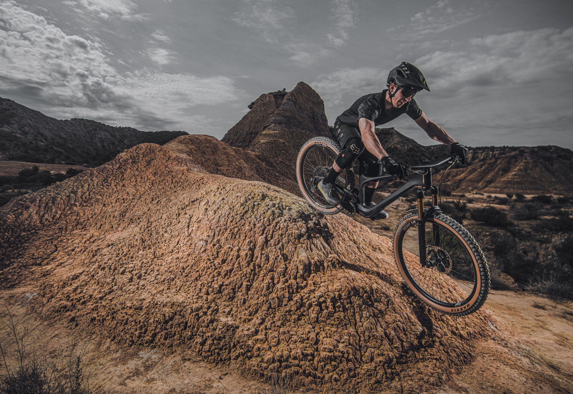 Biker fährt über braunen Dirt-Hügel in steiniger Landschaft