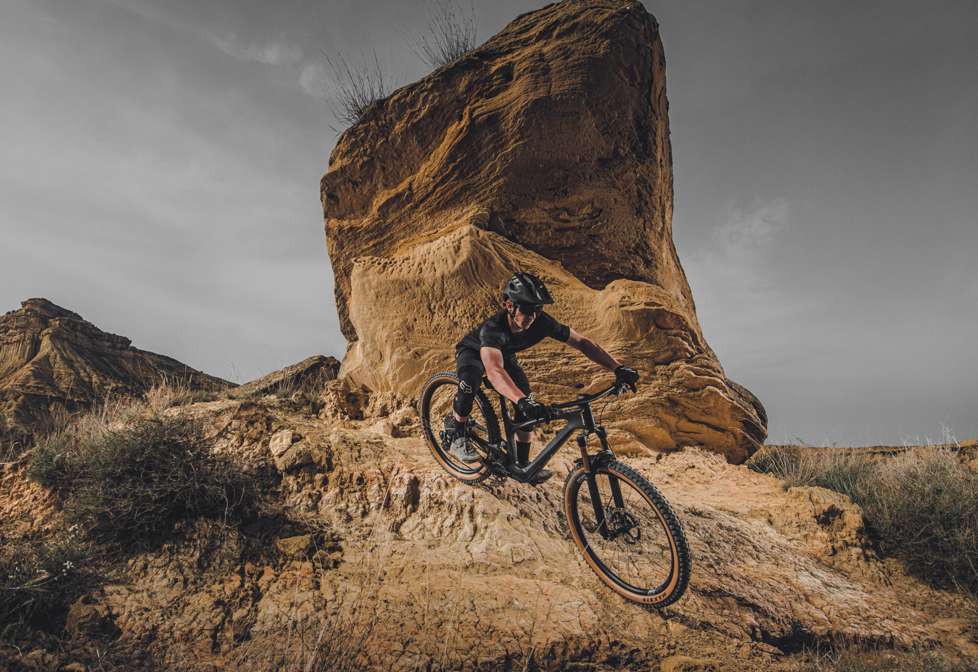 Biker fährt über Schotterhügel vor eindrücklicher Kulisse (grosser allein stehender Fels)