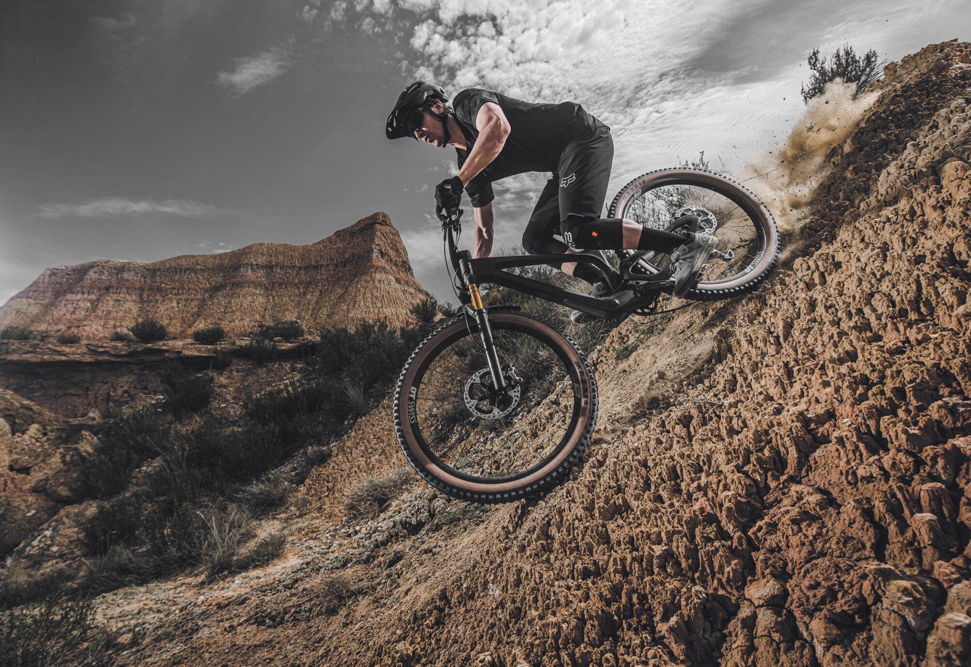 Biker fährt dynamisch steinigen Hügel hinab in Macchia-Landschaft Spaniens
